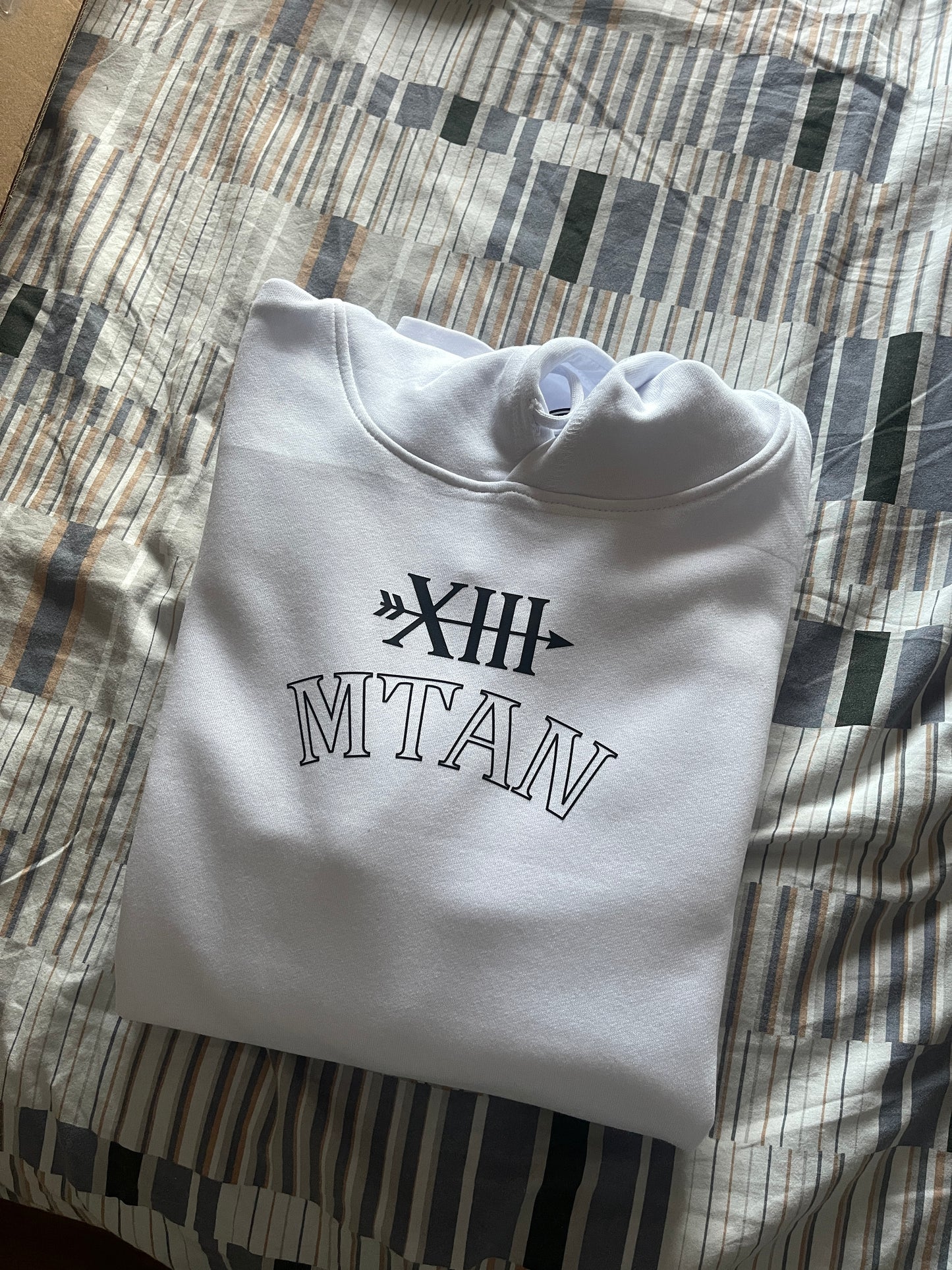 Folded white hoodie with black text on a patterned surface