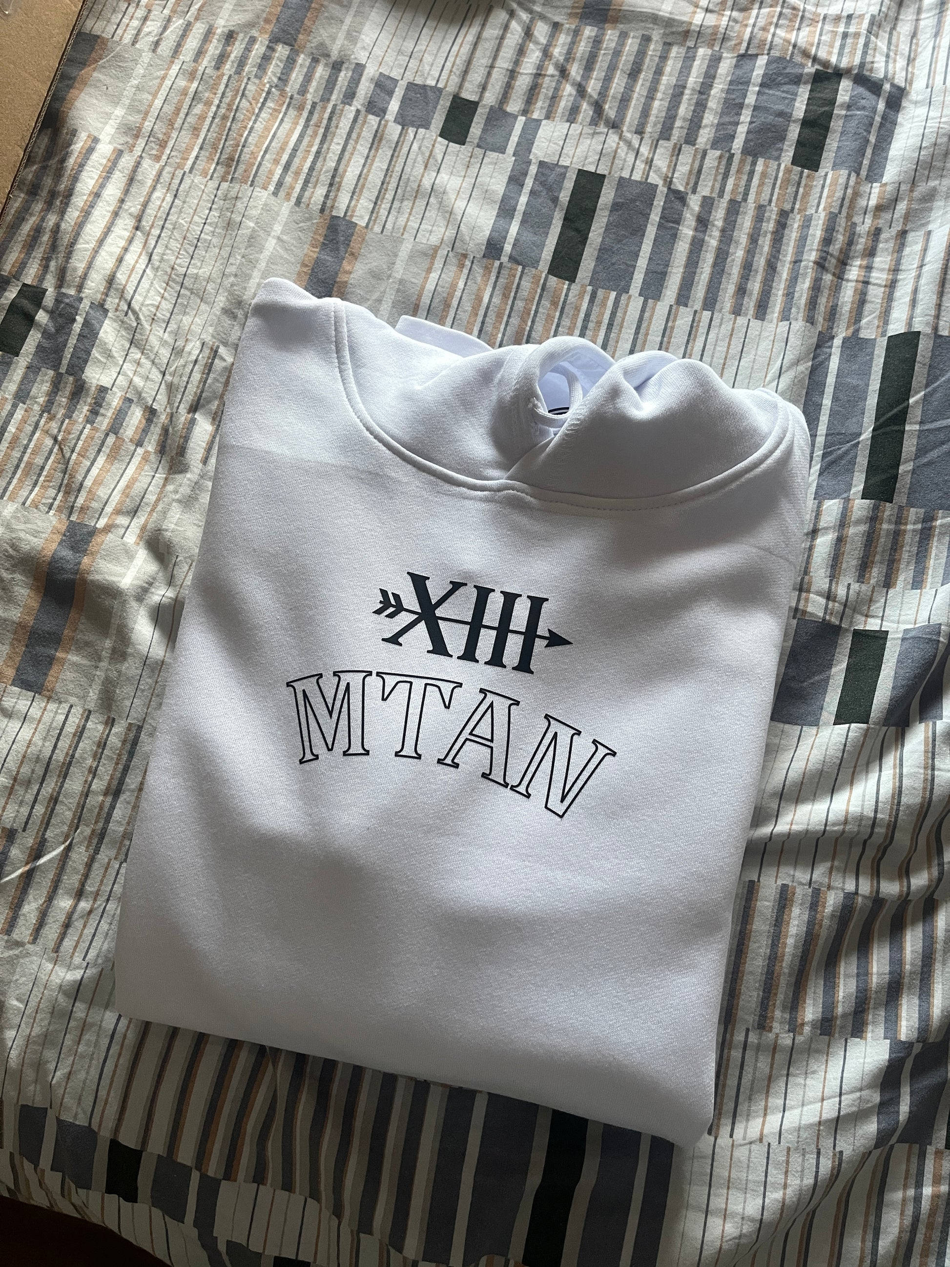 Folded white hoodie with black text on a patterned surface