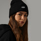 Woman wearing MTAN black beanie with a logo on a gray background
